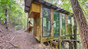 Uma cabana de madeira com janelas amplas, cercada por árvores e um caminho de terra.