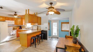 A kitchen with wooden cabinets, a central island with stools, a ceiling fan, and a dining area with a wooden table and chairs. - Steps to Lake Erie! Cedar Point Home Base w/ Deck (Sandusky)