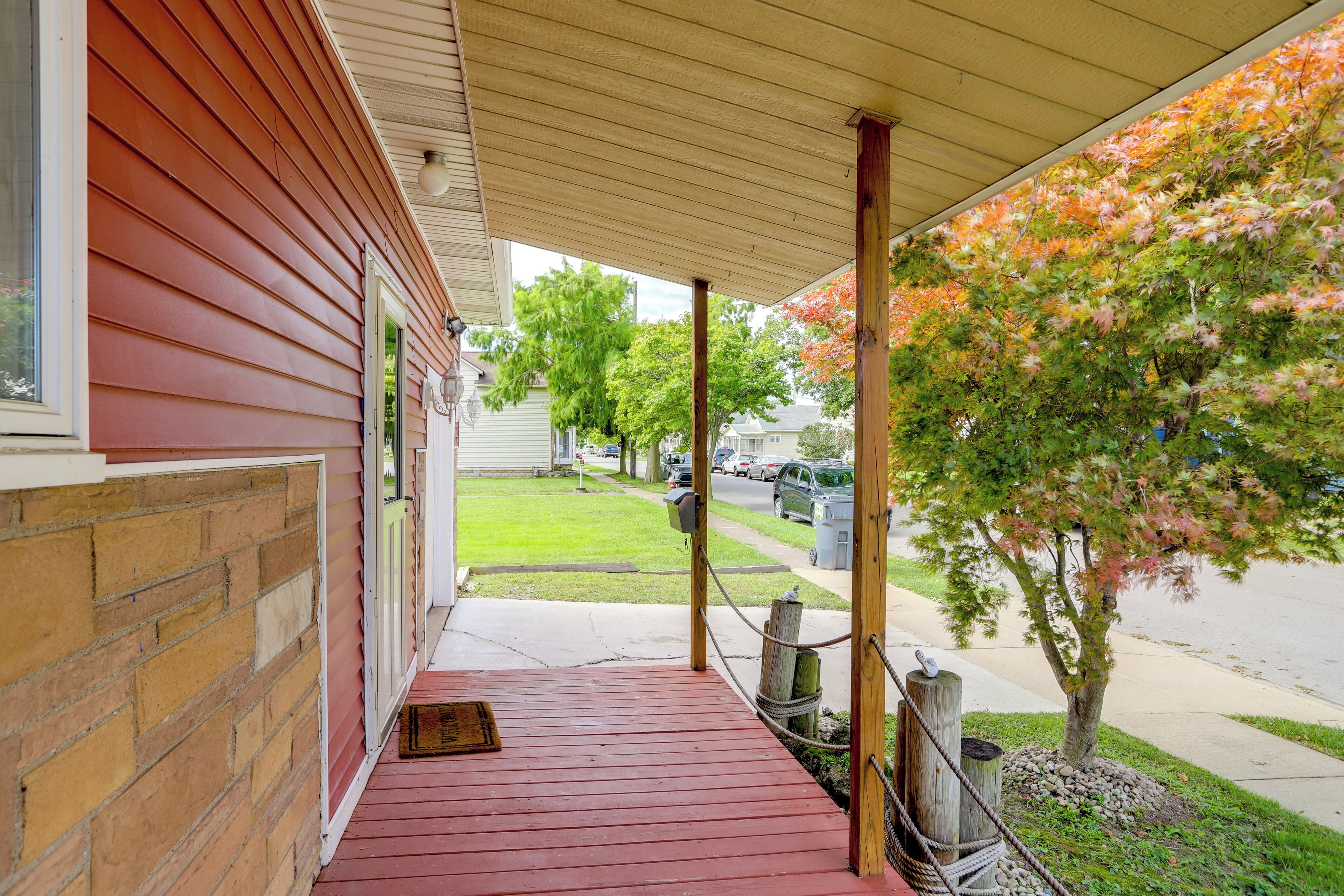A covered porch with a red floor, wooden columns, and a view of a street with cars and trees.