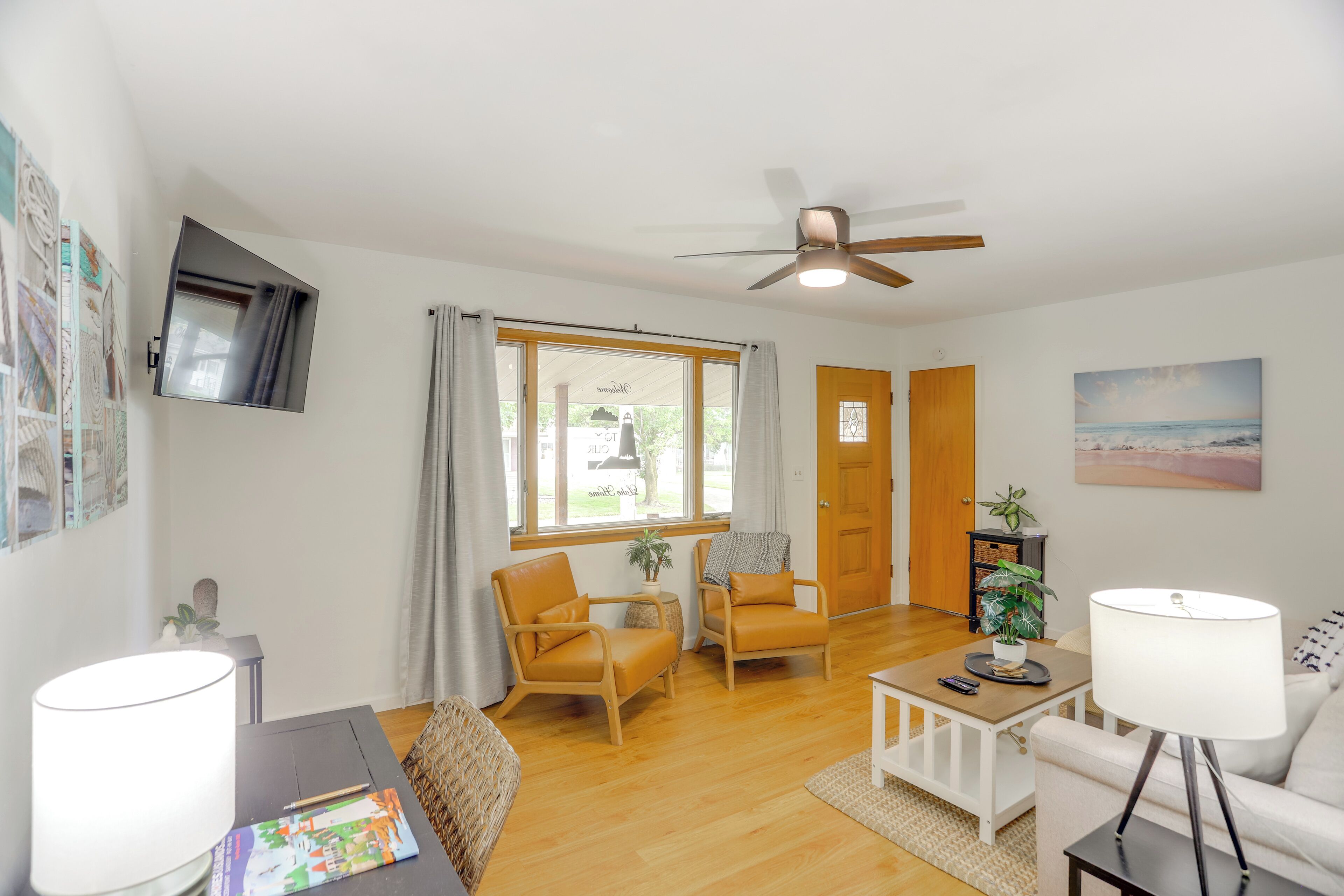 A well-lit living room with a ceiling fan, two chairs, a small table, a lamp, and a painting on the wall.
