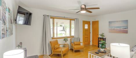 A well-lit living room with a ceiling fan, two chairs, a small table, a lamp, and a painting on the wall.