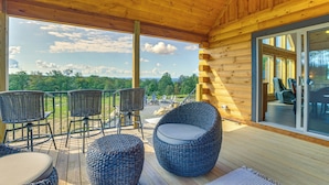 Una terraza de madera con mobiliario de mimbre y un ventanal que da a un espacio interior.