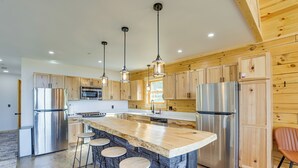 Una cocina moderna con armarios de madera, electrodomésticos de acero inoxidable, una isla central con taburetes e iluminación colgante.