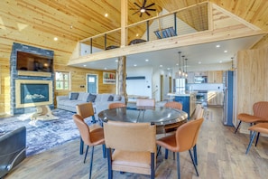 A spacious living area with a fireplace, a round dining table, and a loft bedroom with a balcony.