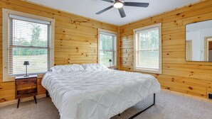 Un dormitorio con cama, paredes de madera, ventilador de techo y ventanas con persianas.
