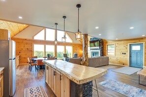 A spacious kitchen with wooden walls, a large island, and a stone fireplace. - Mtn Cabin w/ Hot Tub + Game Room in Mchenry (McHenry)