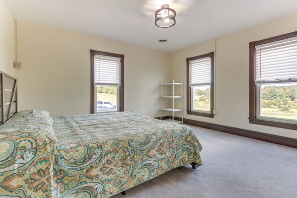 A bedroom with a bed, two windows with blinds, a ceiling light, and a white shelf unit. - Golf Course Guest Suite in Gettysburg (Gettysburg)