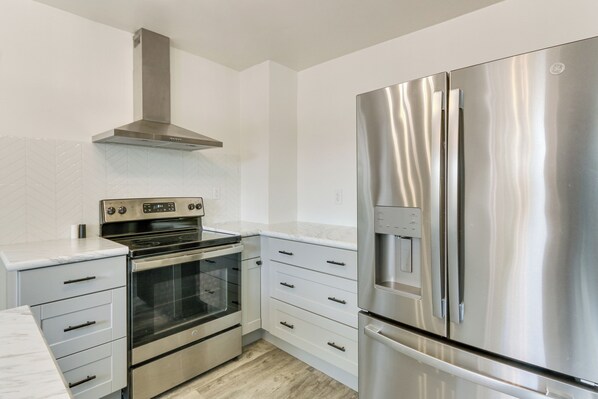 Une cuisine moderne dotée d’appareils électroménagers en acier inoxydable, de meubles blancs et d’un dosseret en carreaux disposés en motif chevron.