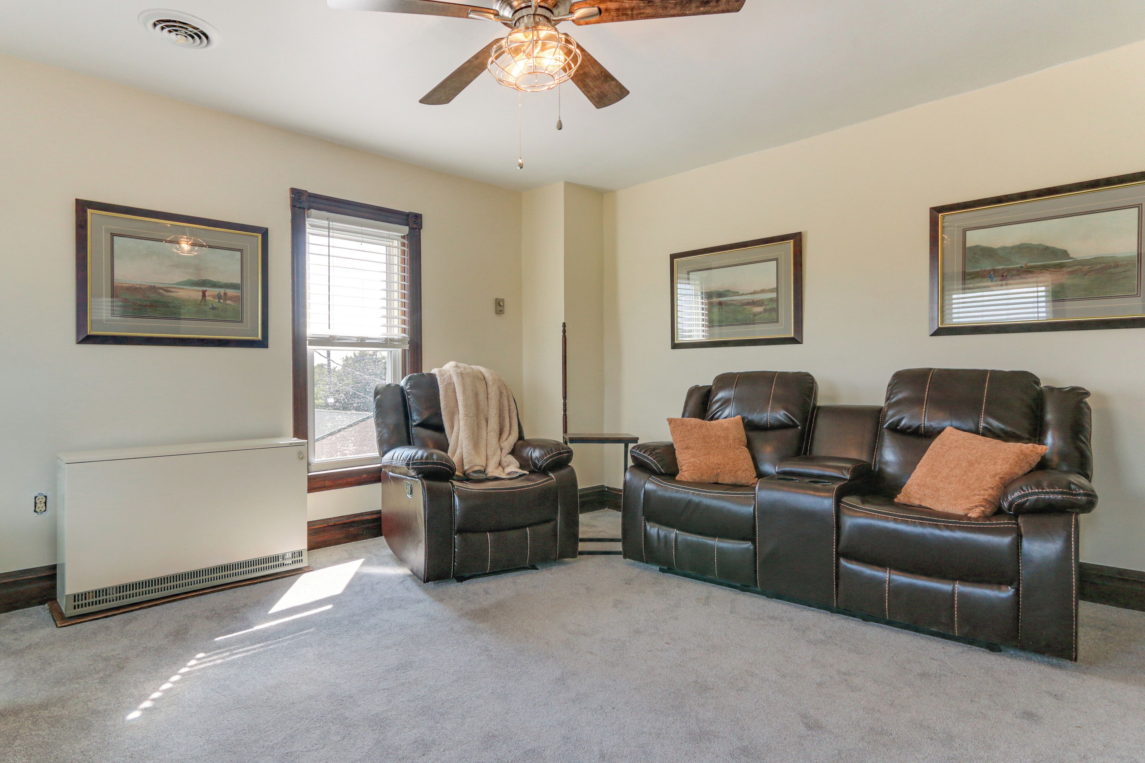 A living room with two leather recliners, a ceiling fan, and framed landscape paintings on the walls.