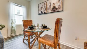 A dining area with a glass table, wicker chairs, and a cityscape painting on the wall. - Screened Patio: Townhome 3 Mi to Dtwn Wilson! (Wilson)