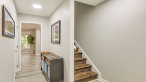 A hallway with a wooden staircase, a cabinet with books, and framed pictures on the walls. - 2 Mi to Tiger Territory! Condo w/ Community Pool (Auburn)