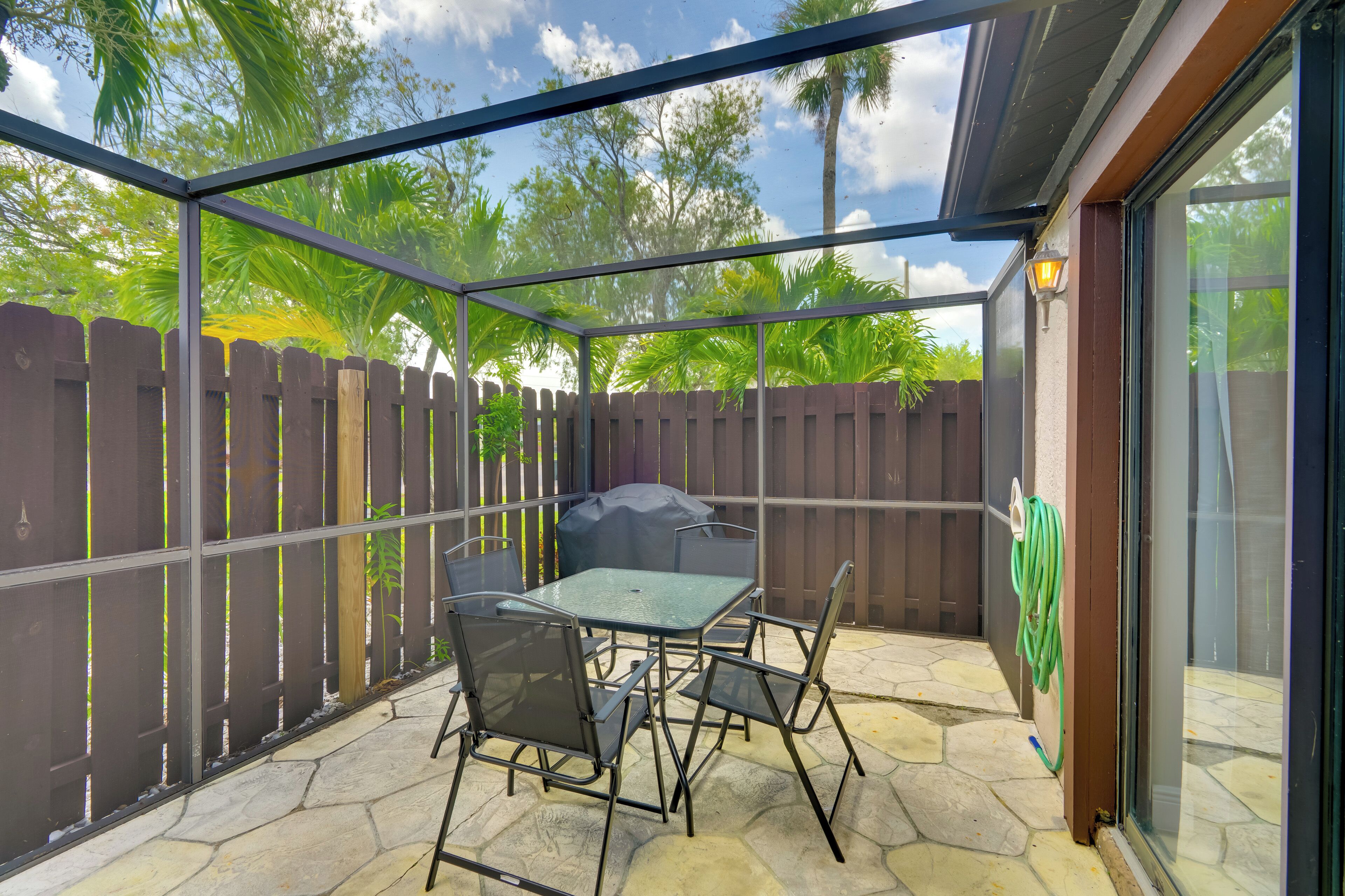 An outdoor patio with a glass enclosure, a table, chairs, a barbecue grill, and a wooden fence.