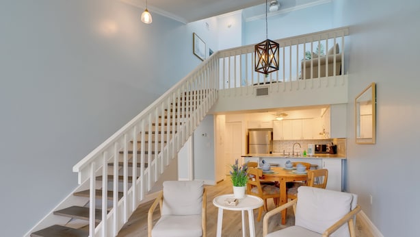 A staircase with white railings leading to a second floor, a dining area with a table and chairs, and a kitchen visible through an open door.
