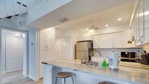A modern kitchen with white cabinets, a stainless steel refrigerator, a built-in oven, a microwave, and a large island with stools.