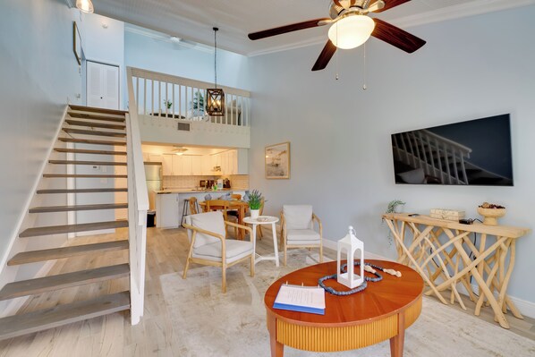 Un vaste espace de vie agrémenté d’un escalier en bois, d’une table à manger avec des chaises, d’un ventilateur de plafond et d’une cuisine en arrière-plan.