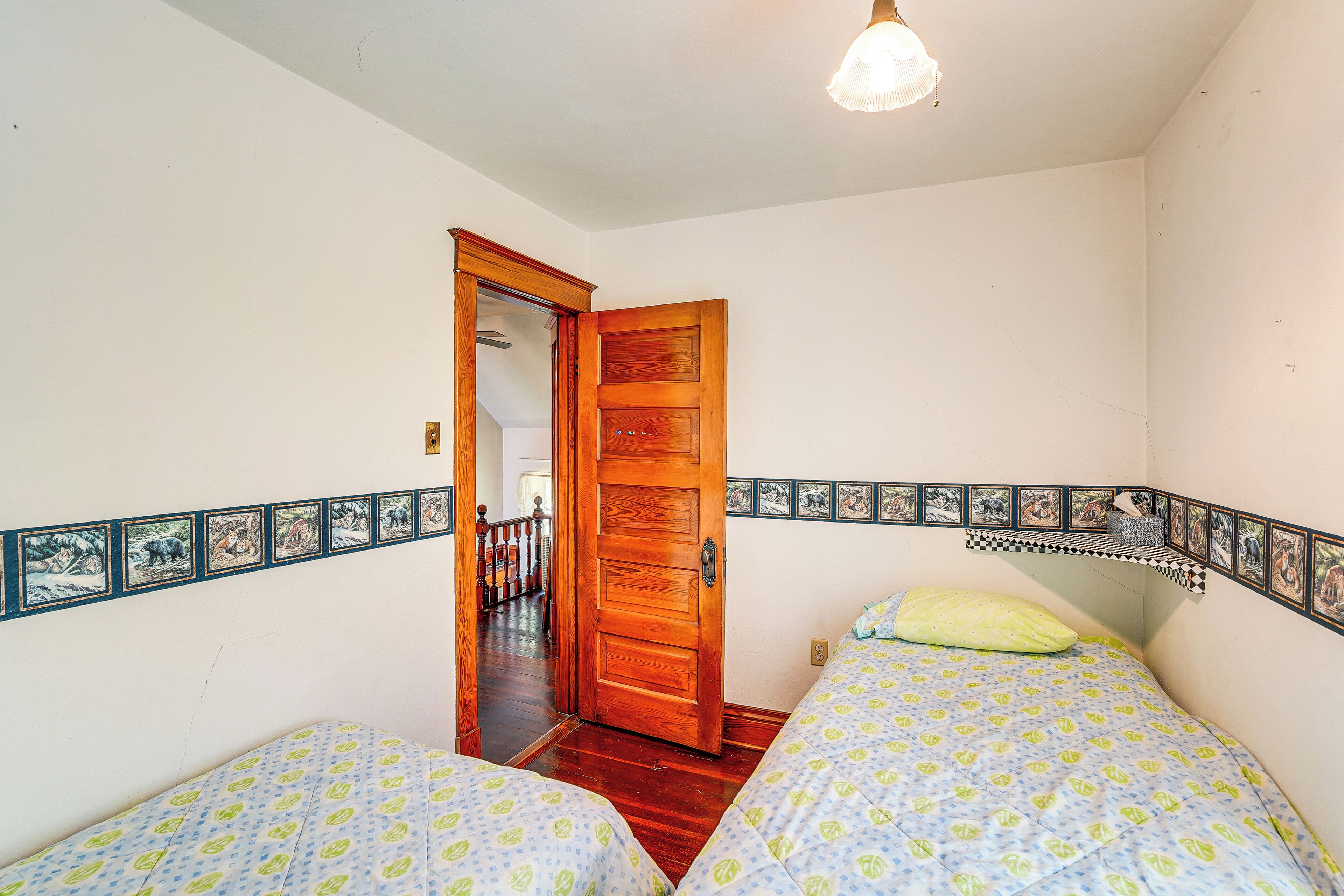 Quarto com duas camas, uma porta de madeira e um corredor que dá para uma escada.
