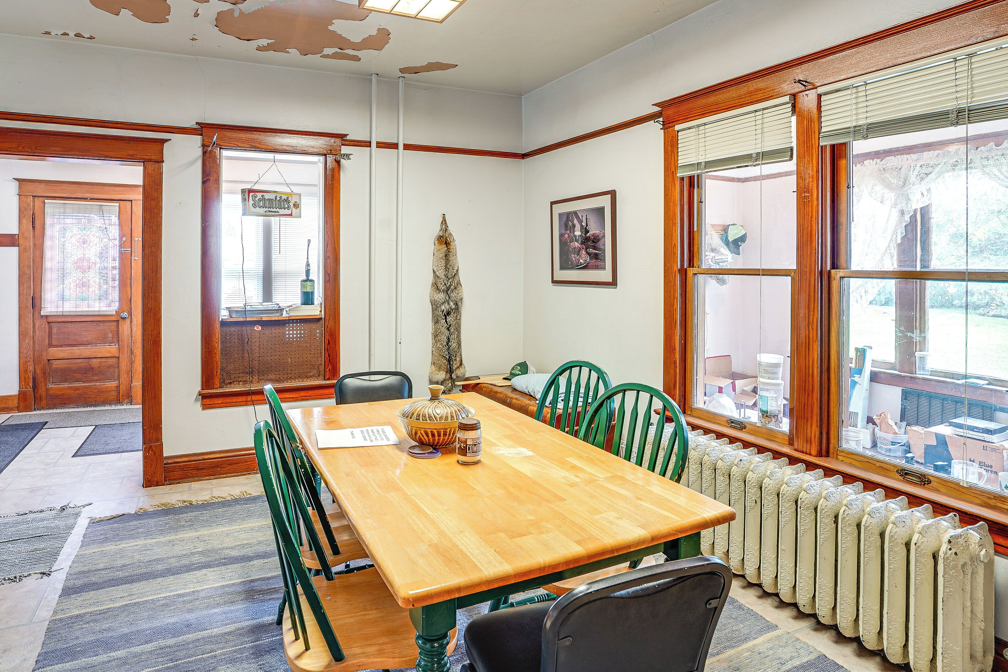 A dining area with a wooden table, green chairs, a radiator, and large windows with blinds.