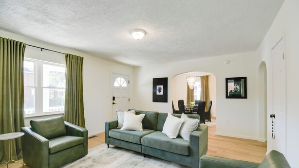 A living room with a green sofa, a small side table, and a large window with curtains. - Walk to Ritter Park: Renovated Home Near Marshall! (Huntington)
