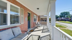 A covered porch with a white railing, a grey sofa, and a door with a green wreath. - Walk to Ritter Park: Renovated Home Near Marshall! (Huntington)