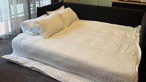 Una habitación de hotel con cama, mesita de noche, ventana con cortinas y puerta.