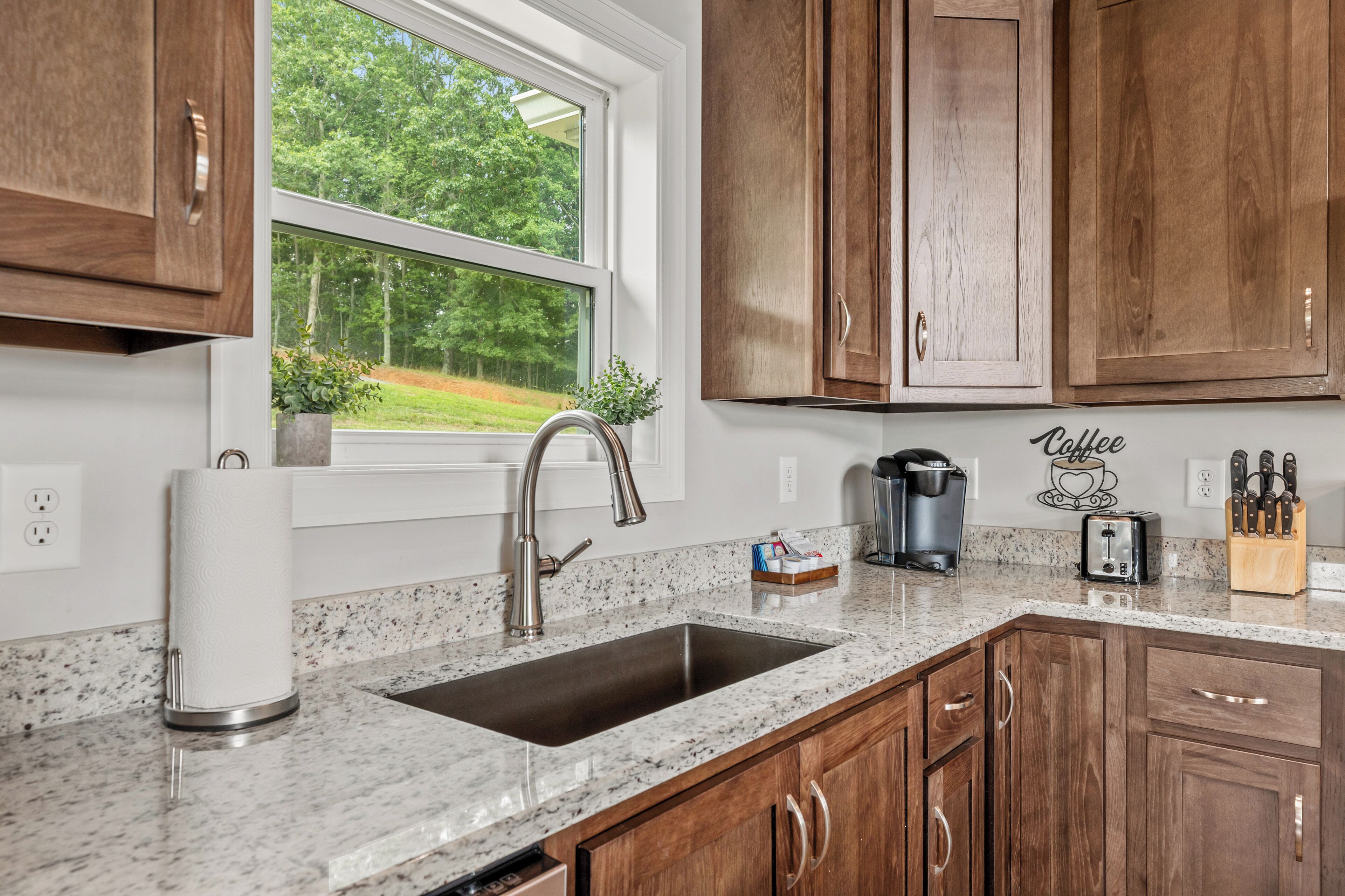 A kitchen with a granite countertop, stainless steel sink, and wooden cabinets.