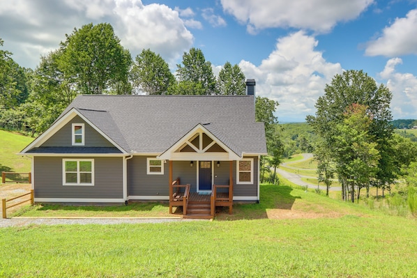 A two-story house with a porch, a chimney, and a view of a green landscape. - Cozy Blue Ridge Cabin: Game Room & Mountain Views (Blairsville)
