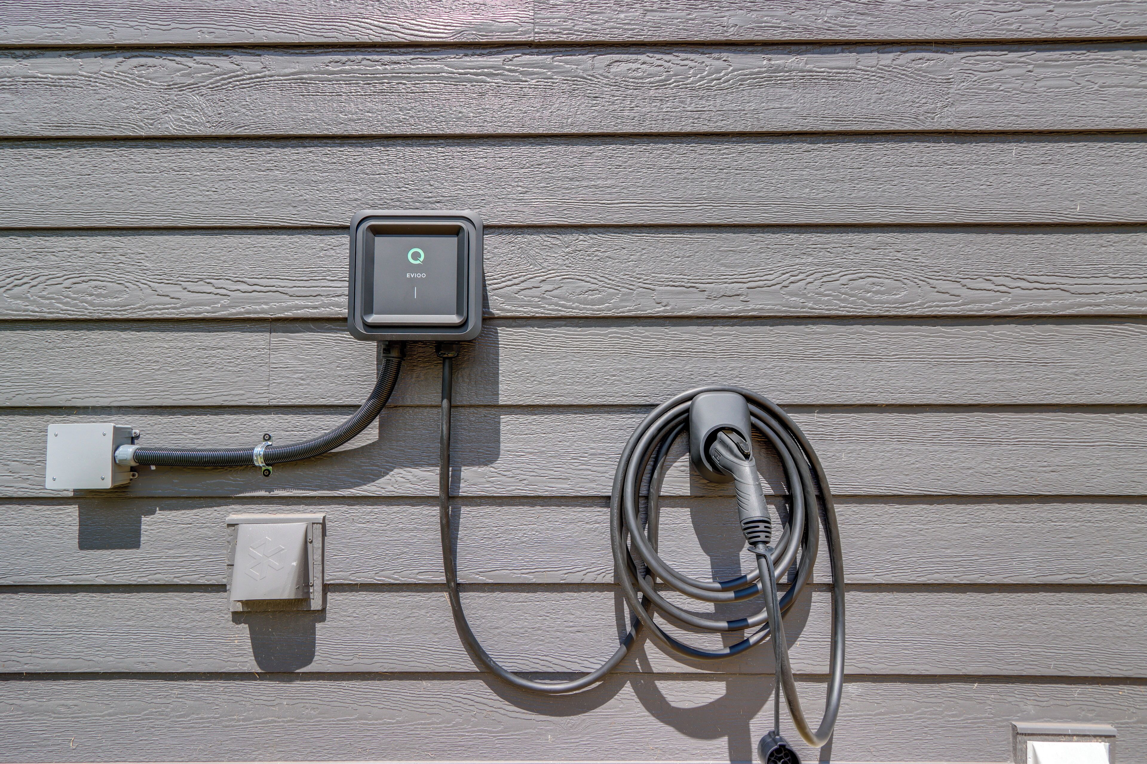 Une borne de recharge pour véhicules électriques fixée à une maison, avec un câble qui y est raccordé.