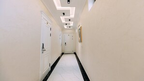 Ein Korridor mit weißen Wänden, schwarz-weißer Fliesenoptik und eingelassener Beleuchtung.