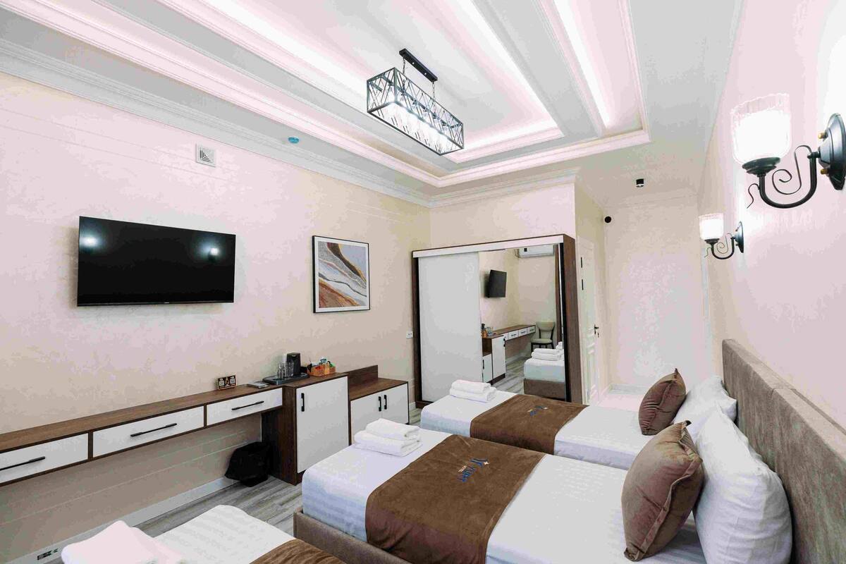 A hotel room with two beds, a desk with a flat-screen TV, a mirror, and a ceiling light fixture.