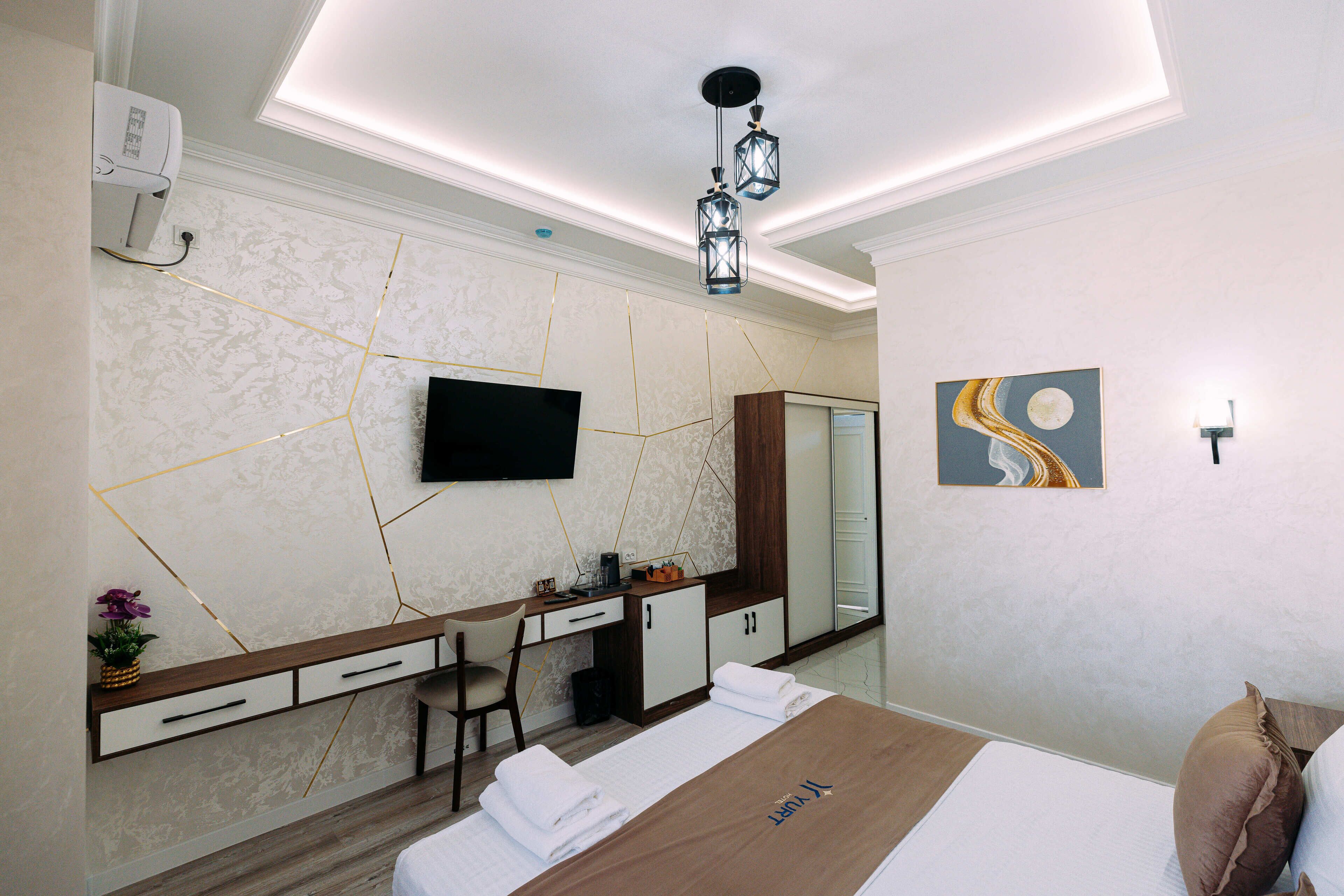 A modern hotel room with a bed, a desk, a chair, a flat-screen TV, and a mirror.