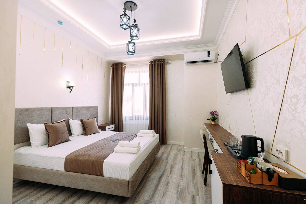 A hotel room with a large bed, a desk, a television, and a window with curtains.
