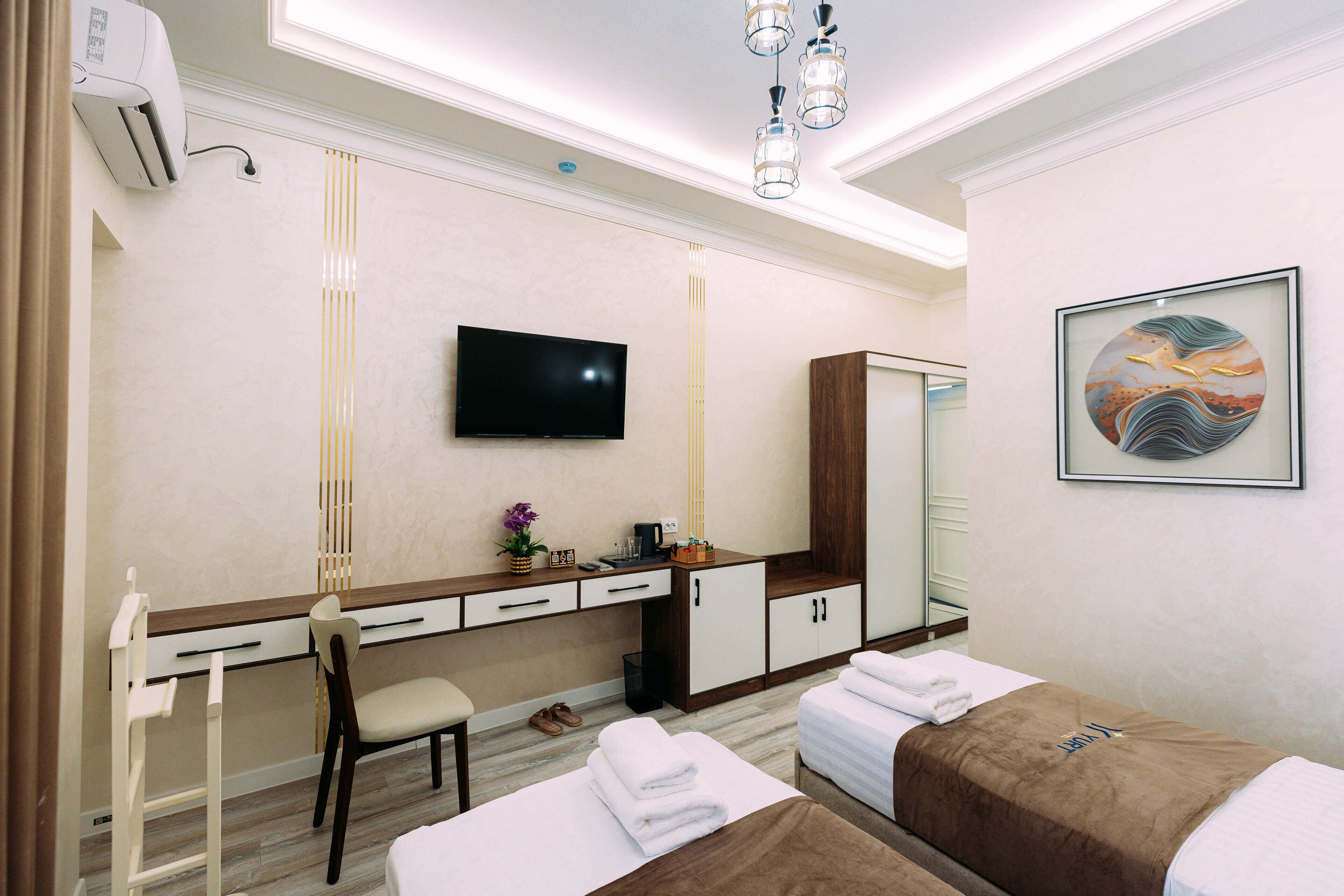 A hotel room with a desk, two beds, a TV, a mirror, and a painting.