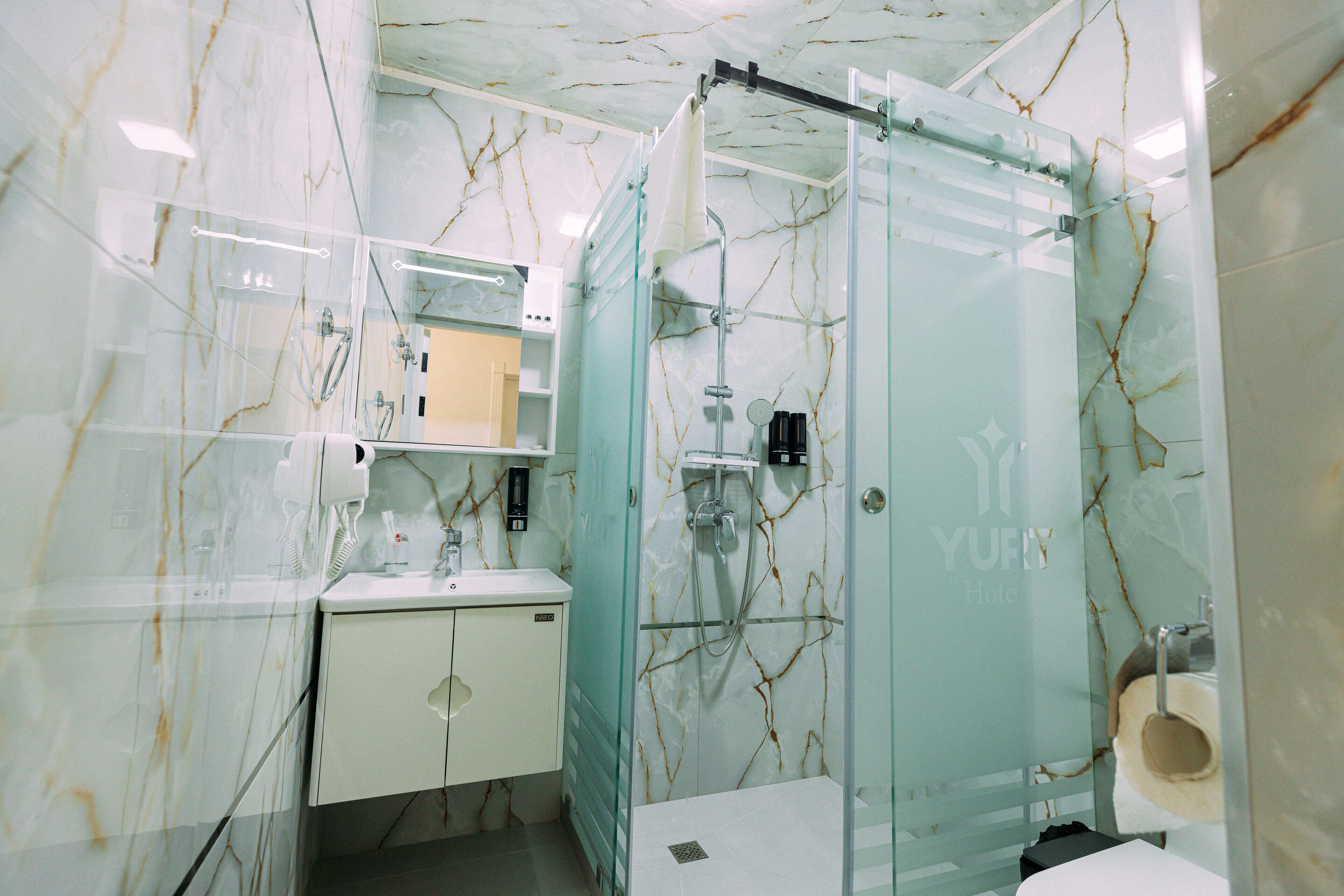 A modern bathroom with a glass-enclosed shower, a white sink, and a marble-patterned wall.