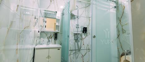 A modern bathroom with a glass-enclosed shower, a white sink, and a marble-patterned wall.
