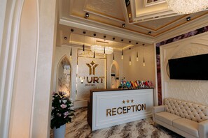 A reception area with a marble floor, a reception desk, a chandelier, and a sofa. - Yurt (Samarkand)