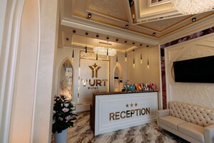 Un área de recepción con suelo de mármol, mostrador de recepción, candelabro y un sofá.