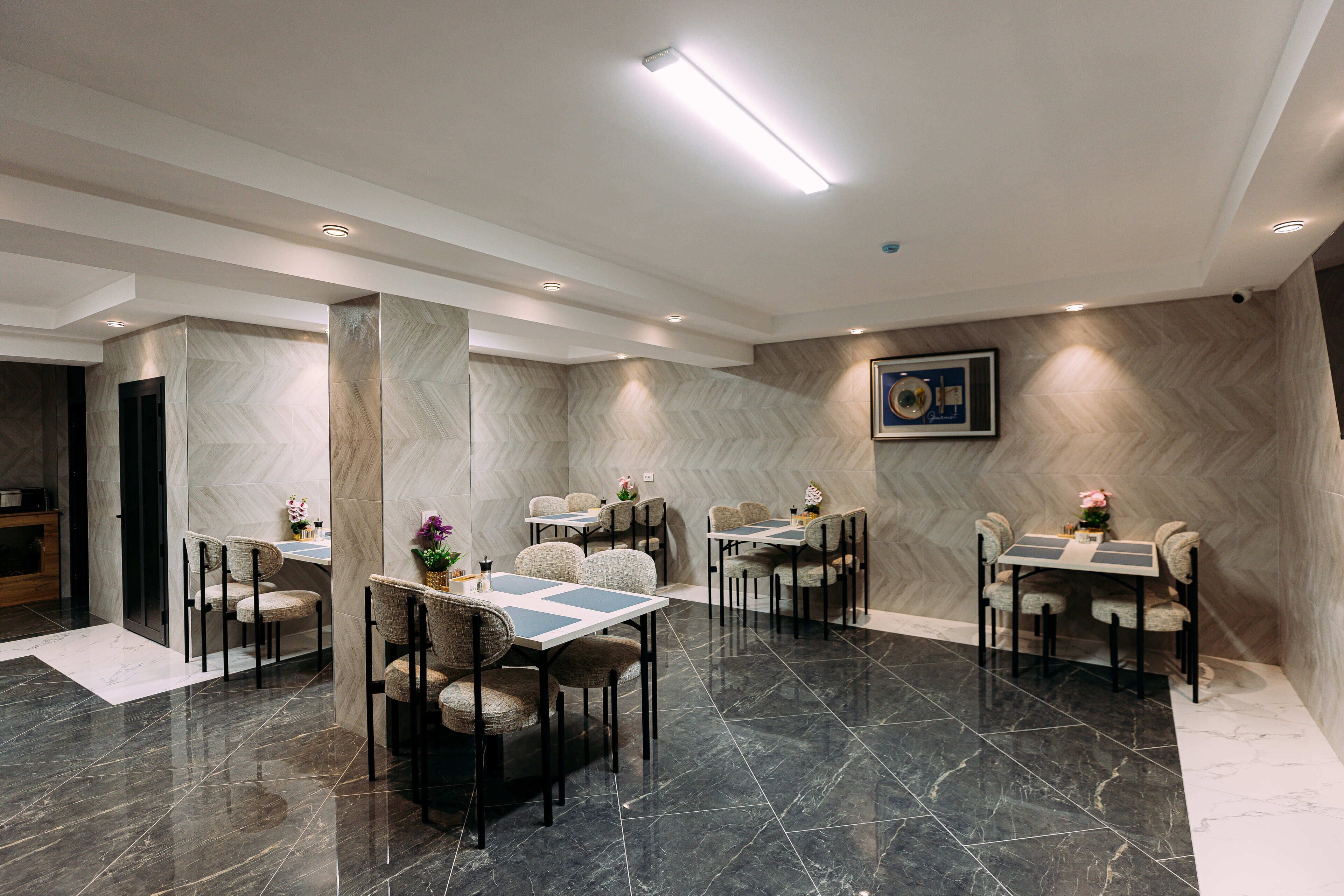 A modern dining area with marble flooring, multiple tables and chairs, and recessed ceiling lighting.