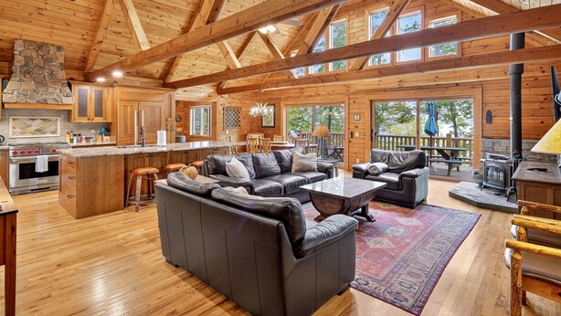 Amplia sala de estar con chimenea, sofá de cuero y comedor con mesas y sillas de madera.