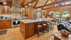 Una cocina amplia con armarios de madera, una isla grande con taburetes, una chimenea de piedra y vistas al exterior.