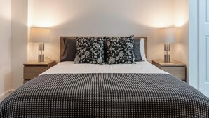 A neatly made bed with a patterned bedspread, two decorative pillows, and two bedside lamps on wooden nightstands.
