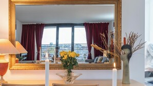 A hotel room with a large mirror, a desk with chairs, a vase with yellow flowers, a candle, and a decorative sculpture.
