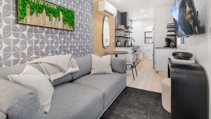 A modern living room with a grey sofa, a cityscape artwork, and a kitchen area in the background.