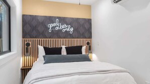 Une chambre moderne avec un lit, une tête de lit ornée d’une citation inspirante et une fenêtre.