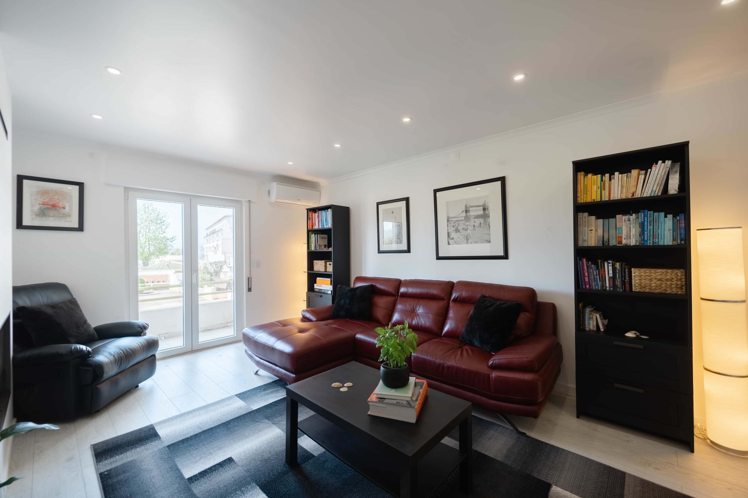 Een woonkamer met een rode leren bank, een zwarte salontafel, een boekenkast en een lamp.