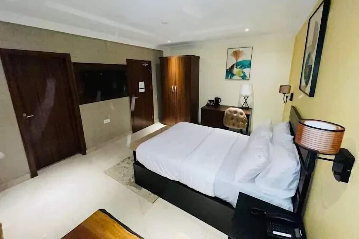A modern hotel room with a large bed, a desk, a chair, and a wardrobe.