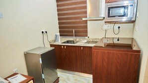 A compact kitchen with a refrigerator, microwave, and wooden cabinets. - Hayatt Regency Suites (Katsina)