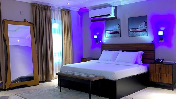 A modern bedroom with a large bed, a mirror, and a nightstand. - Hayatt Regency Suites (Katsina)