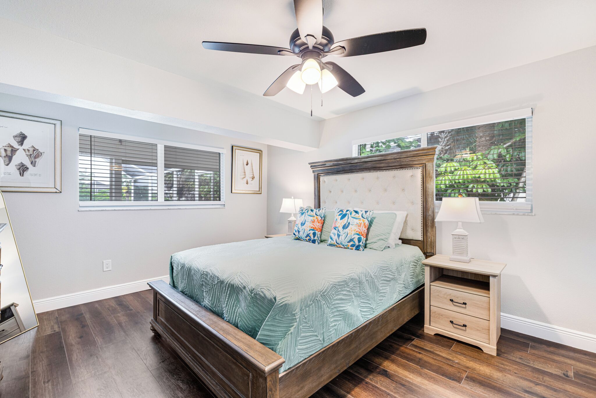 Un dormitorio con cama de madera, ventilador de techo y mesita de noche con lámpara.