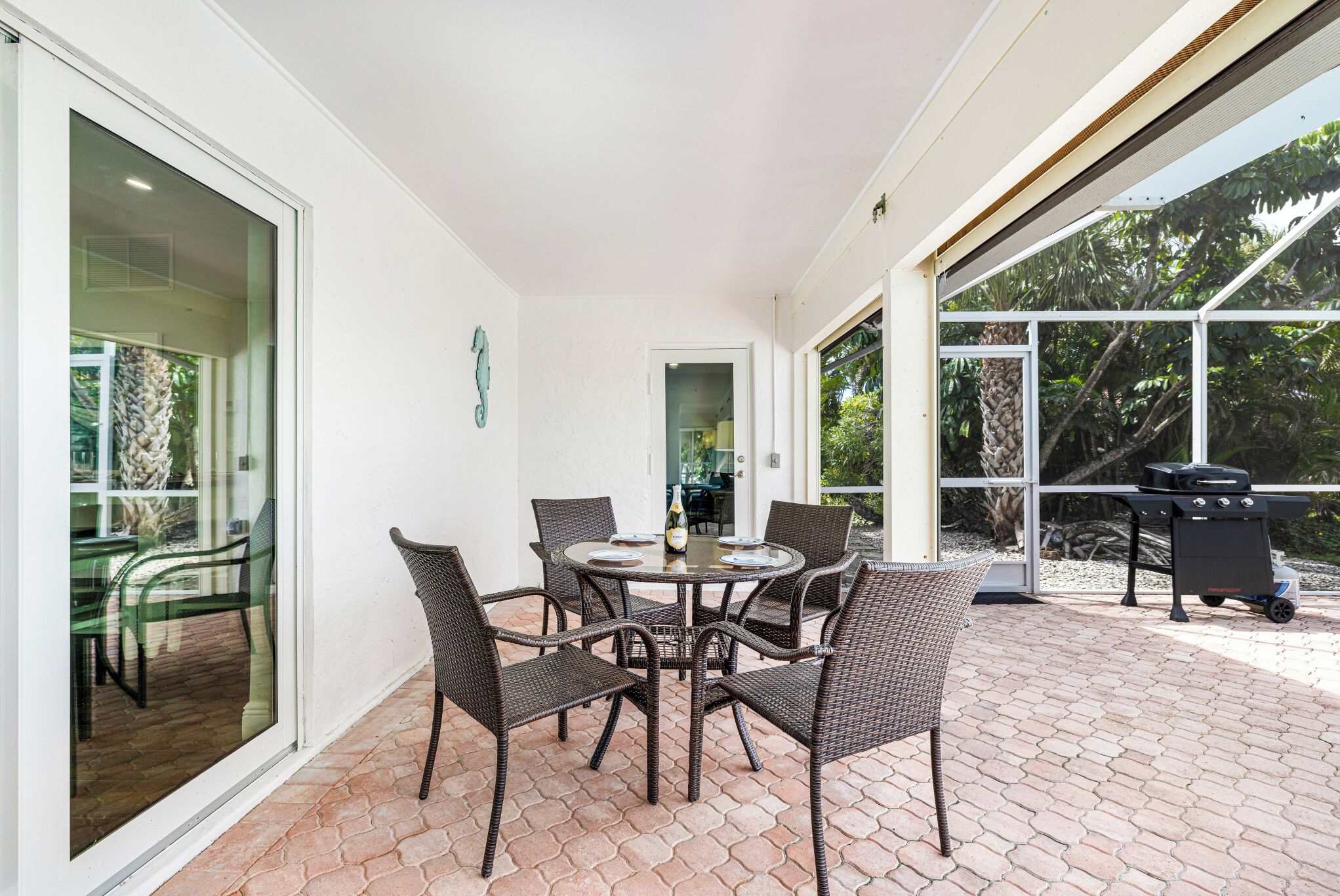 A patio with a round table and wicker chairs, a grill, and a glass door leading to a patio area.