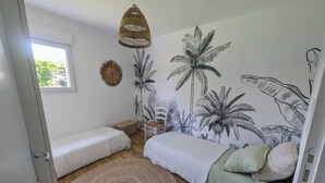 A bedroom with two single beds, a woven rattan chair, a woven floor lamp, a woven wall hanging, and a tropical-themed wall mural. - House with garden, walking distance to the beach (Pornichet)